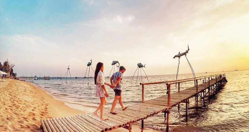 Cặp đôi dạo bước trên cầu gỗ ngắm tượng cá bay Sunset Sanato Phú Quốc